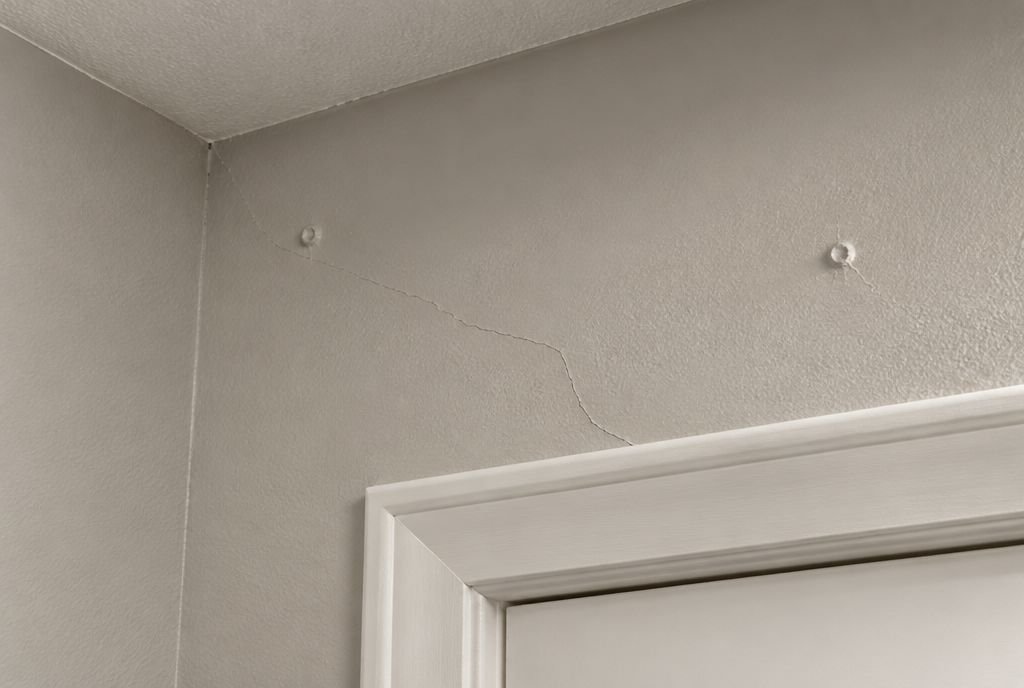 A drywall corner above a door frame showing a hairline crack and nail pops