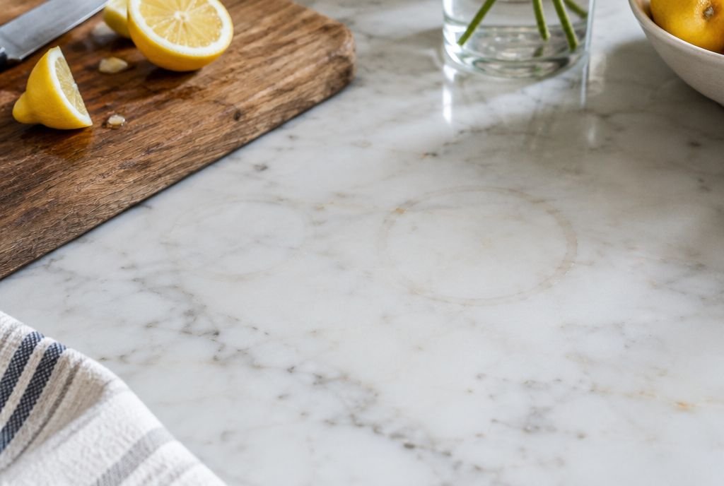 A white marble counter showing a faint dull etch ring next to a cutting board with lemons