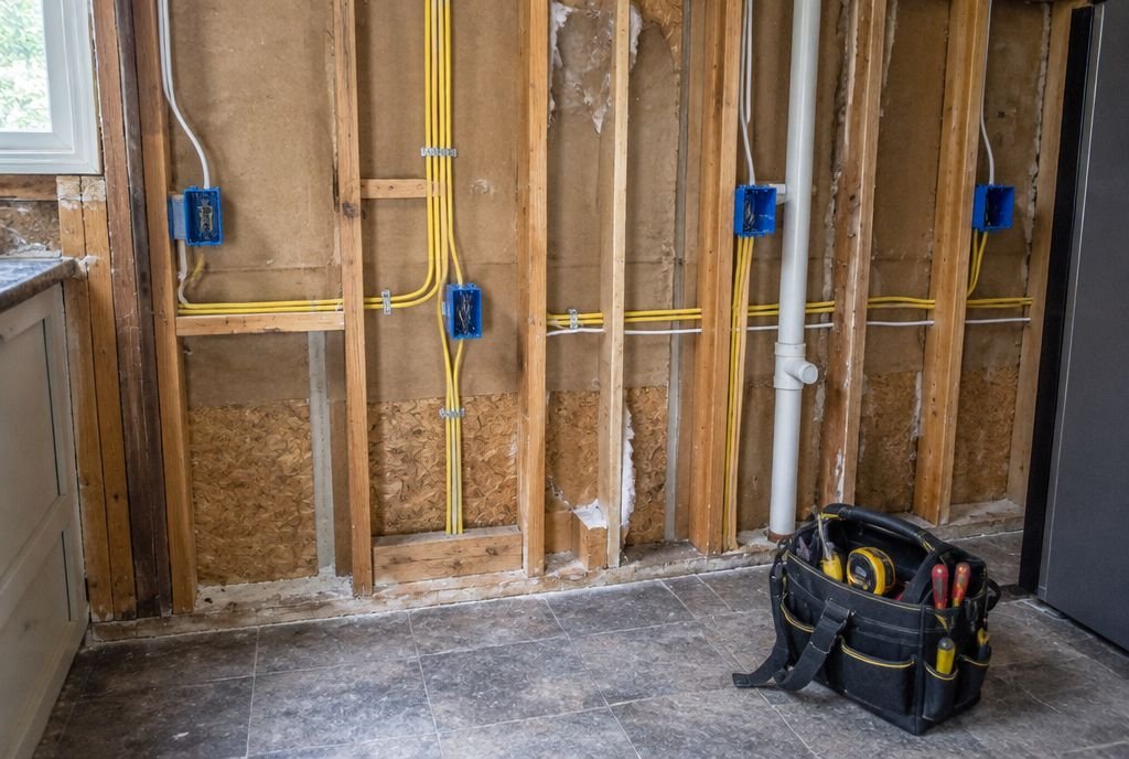 A kitchen wall opened to the studs showing new blue electrical boxes and sheathed cables stapled to studs
